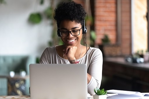 Stock image of a young lady sitting in front of a laptop with headphones on and smiling